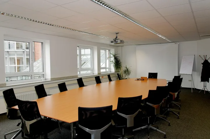 Salón de conferencias con una mesa larga, sillas, proyector y pantalla